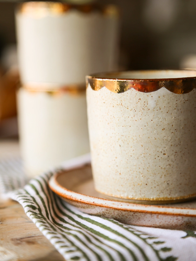  white stoneware drinking beaker with gold scallop decoration around the rim