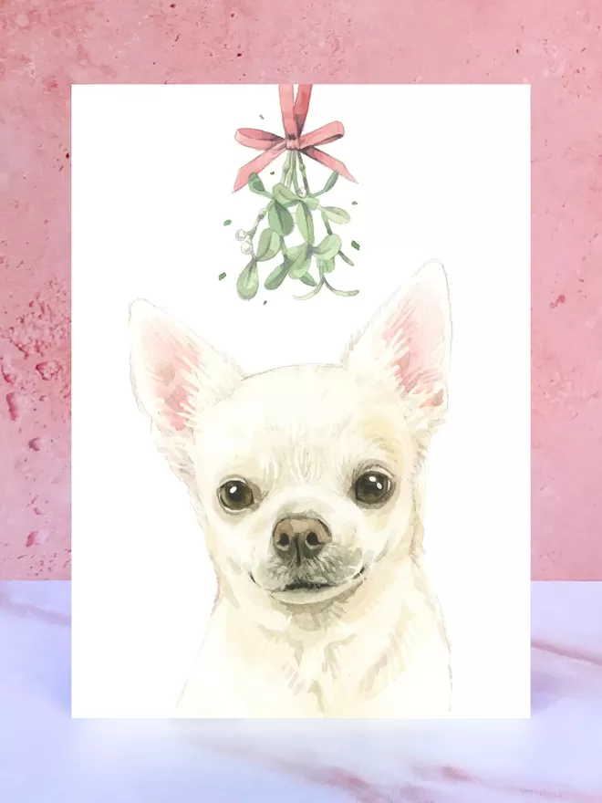A Christmas card featuring a hand painted design of a Chihuahua, stood upright on a marble surface.