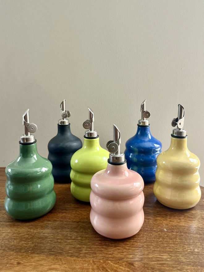 a collection of 6 colourful chubby oil bottles with wavy sides on a wooden table. 