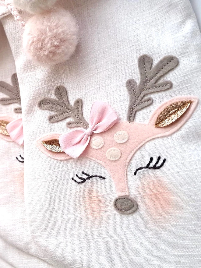 Baby Christmas stocking, close up of felt applique reindeer face with sleepy eyes and pink bow.