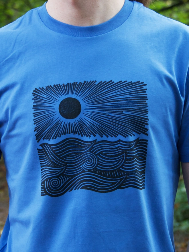 man wearing a blue t-shirt with a black handprinted design on the front depicting the sun and the sea