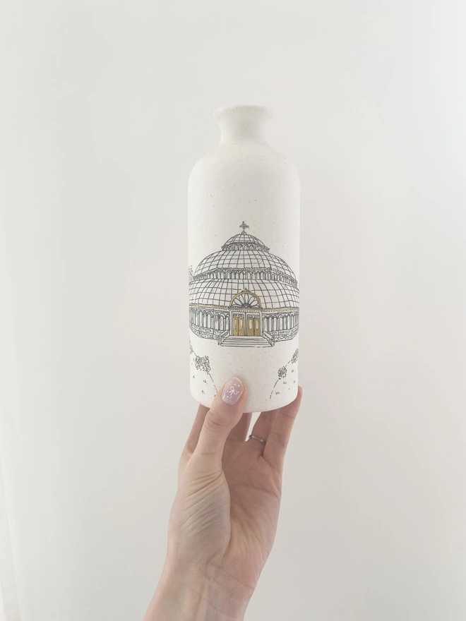 Ceramic vase being held by a woman's hand with black hand drawn venue illustration featuring metallic gold highlights 