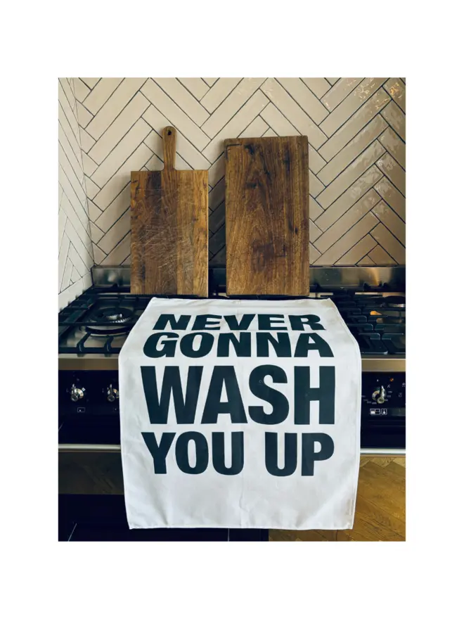 London Drying Never Gonna Wash You Up screenprinted towel laying on stove with chopping boards leaning on tiled wall behind