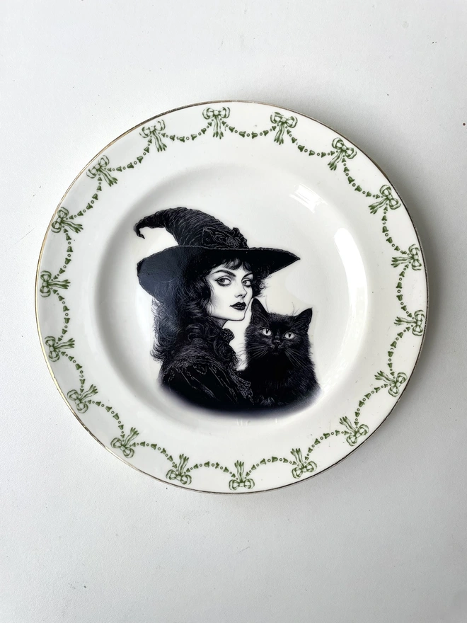 vintage plate with an ornate border, with a printed vintage illustration of a Victorian witch and her black cat in the middle