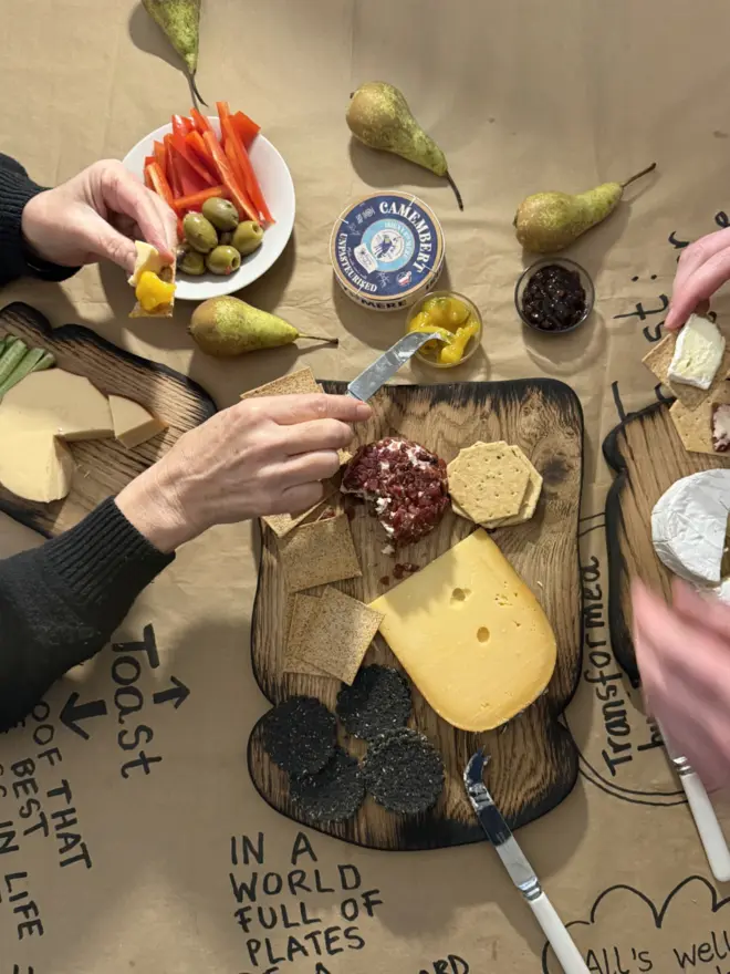 Toast shaped oak chopping board with selection of cheese and crackers on brown paper with toast quotes written on.