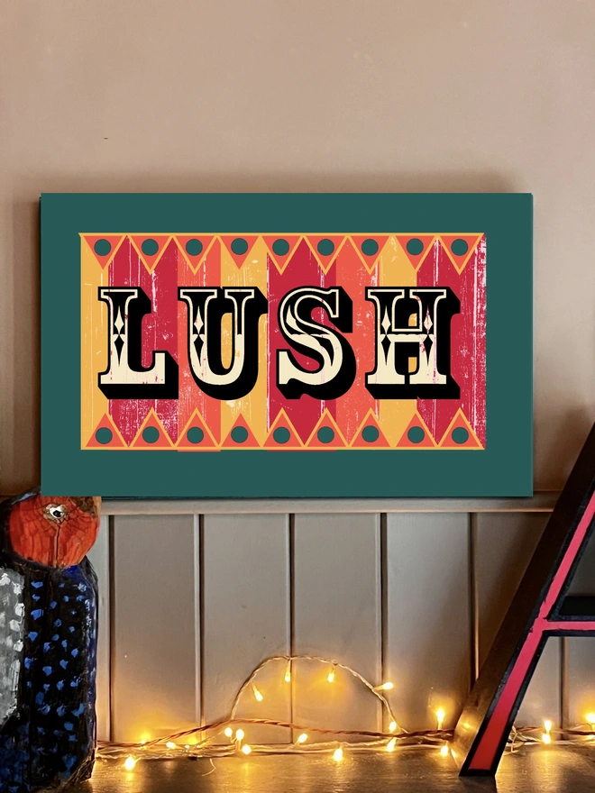 colourful lush sign made from reclaimed wood with a teal frame, hand painted fairground lettering and with orange, pink and yellow stripes, with orange and yellow zig zag patterns  top and bottom