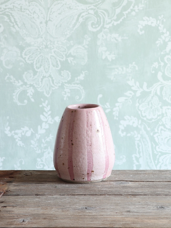 Handmade Ceramic Stoneware Small Vase in Pink sat on a wooden surface against a patterned blue/green wallpaper