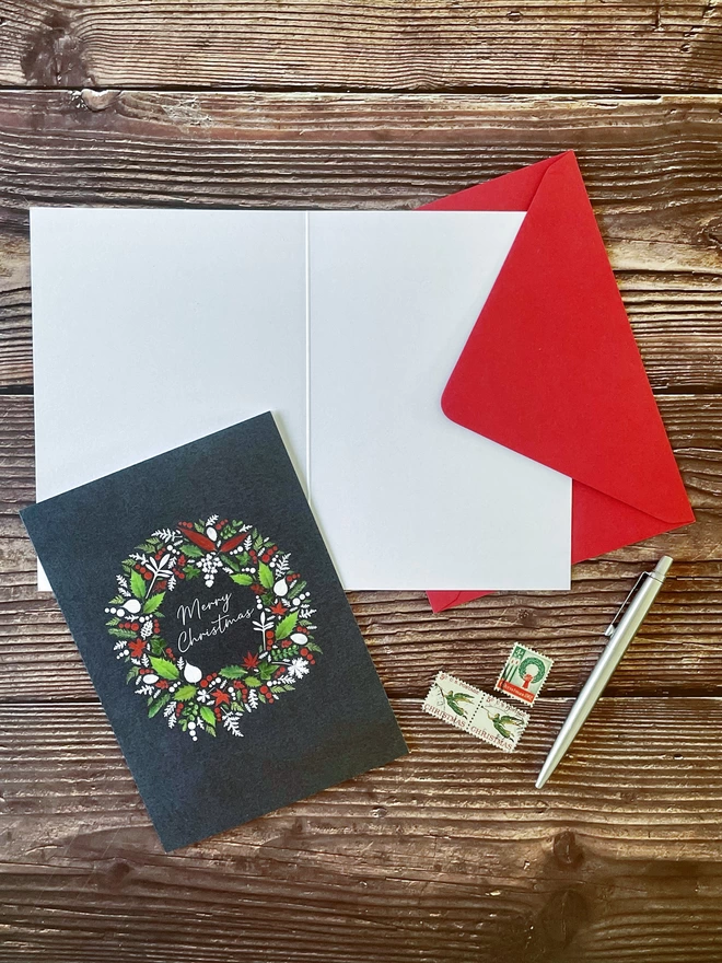 Christmas Card with Wreath Design Made from Pressed Winter Leaves, Holly, and Ivy - Red Envelope - Wooden Background