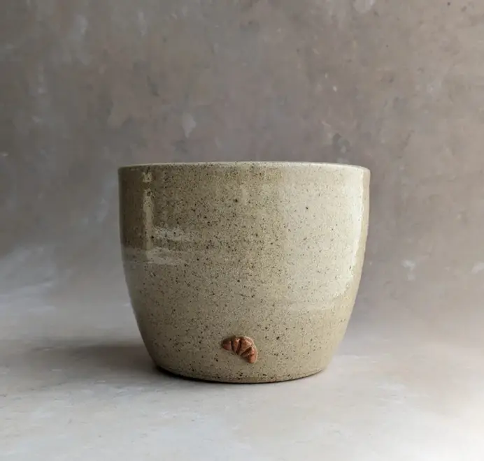 Biscuit colored croissant coffee cup with a subtle croissant design, placed against a grey marble background.