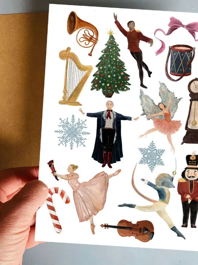 Christmas Temporary Tattoos, a hand holds a white sheet featuring Nutcracker-themed temporary tattoos like a nutcracker, ballerinas, a mouse king, and a Christmas tree.
