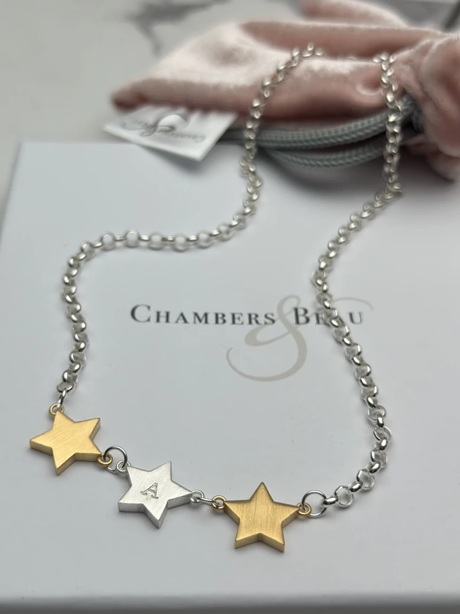 3 chunky star charms hang horizontally from a sterling silver chain.  a personalised silver star hangs in the middle with gold stars on each side