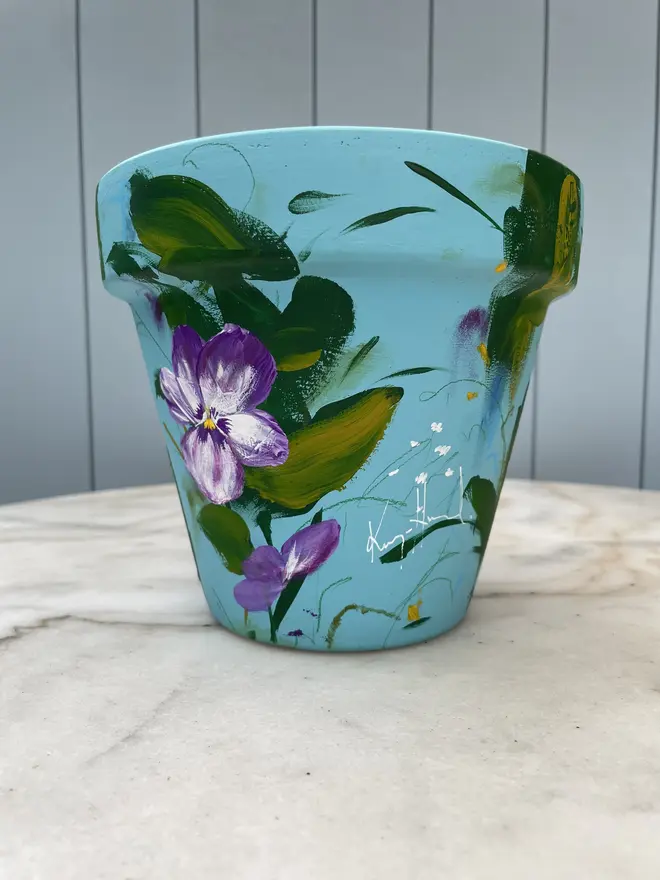 Unique hand-painted terracotta pot featuring purple pansy flowers on a pale blue background