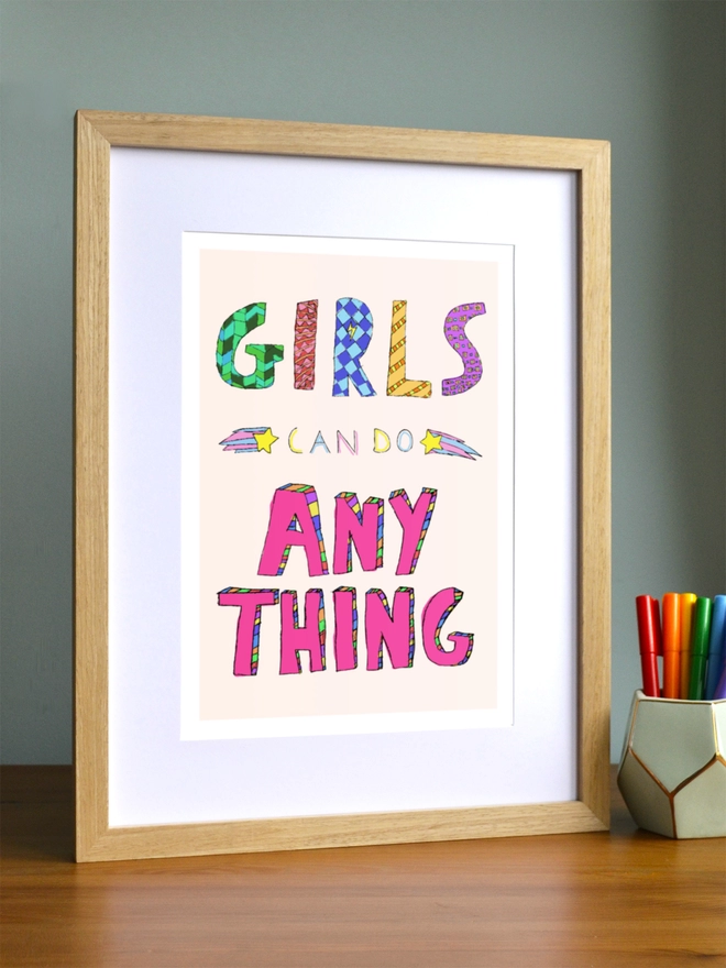 Art print saying 'Girls can do anything' in a brown frame in a child's room