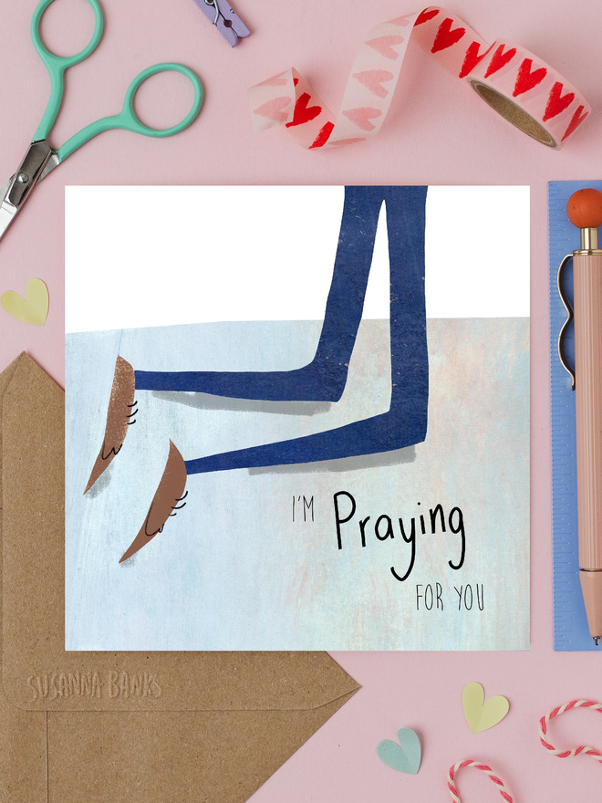 'praying for you' illustrated card. card photographed on table with assorted crafting items.