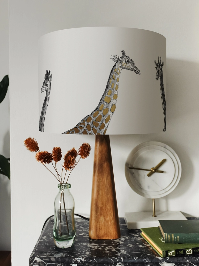 Drum Lampshade featuring Giraffes on a wooden base on a shelf with books and ornaments
