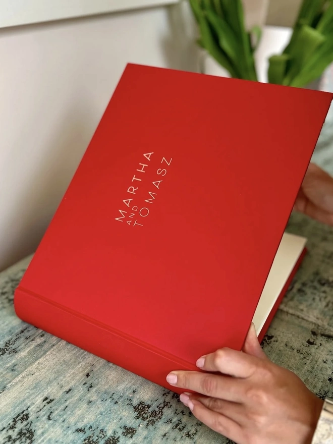 Bold & Beautiful Personalised Guest Book, women opening a red guest book on a wooden surface. 