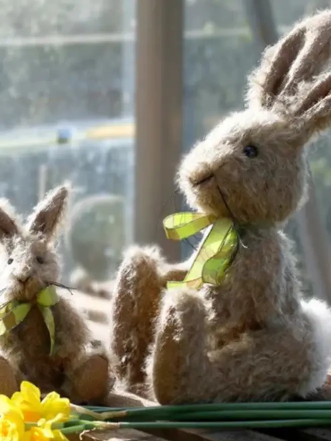 Handmade brown stuffed rabbit with long ears and a green ribbon bow sitting upright with a small bunny against a plain background