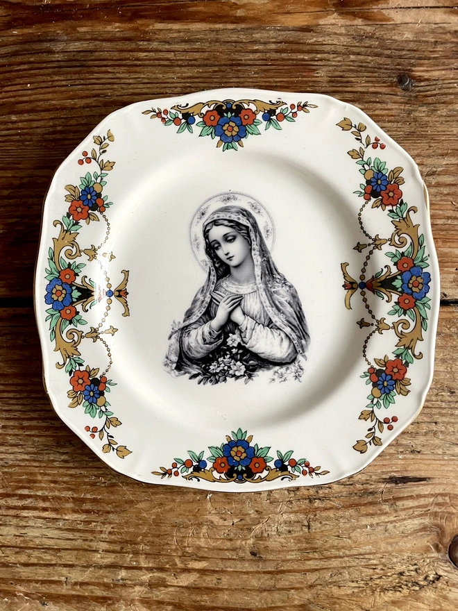 a vintage plate with a really ornate border has the victorian black and white illustration of the virgin mary in the centre