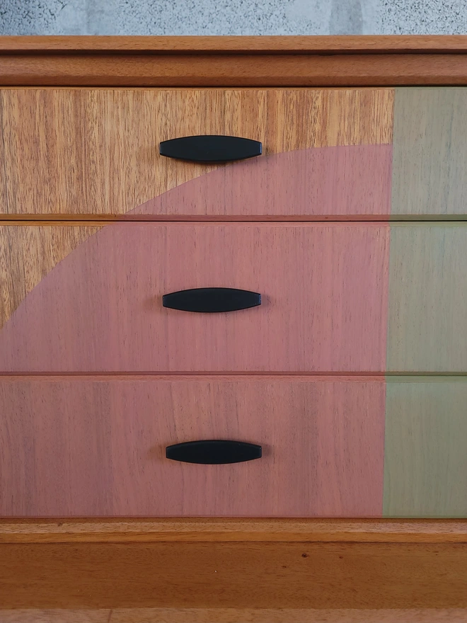 Three teak drawers with translucent pink and green painted shapes and black handles