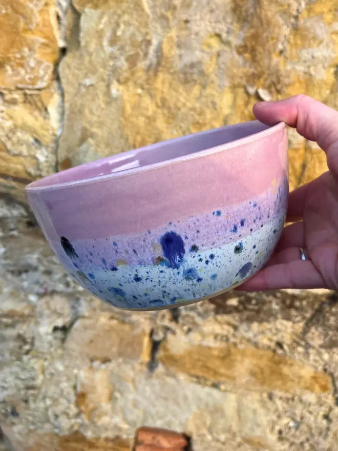 Shoreline Small Bowl, a colourful bowl held in front of a brick wall. 