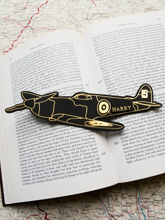 a black leather bookmark with gold illustration of a number nineteen spitfire airplane