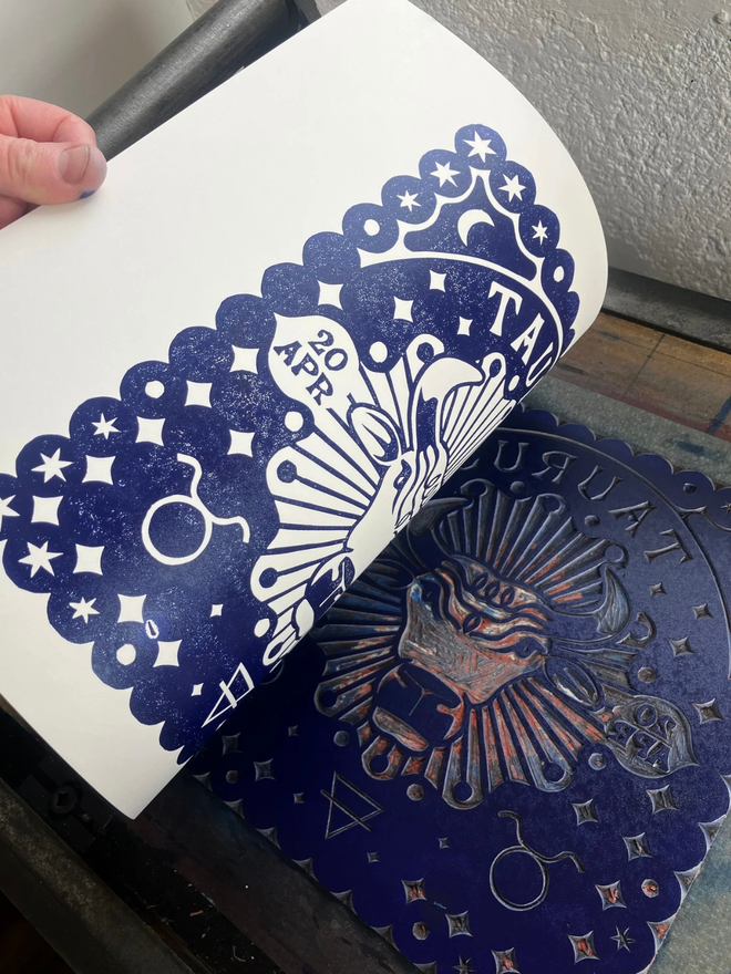taurus zodiac linocut. a bull and zodiac symbols linocut and printed on a blue background.