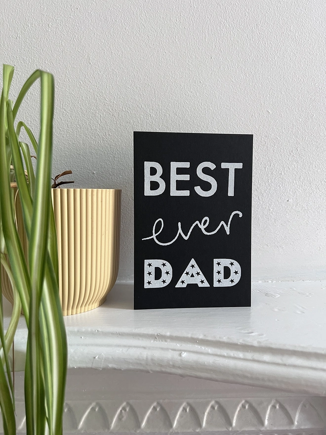 A Mr.PS Best Ever Dad card on a white mantlepiece next to a spider plant
