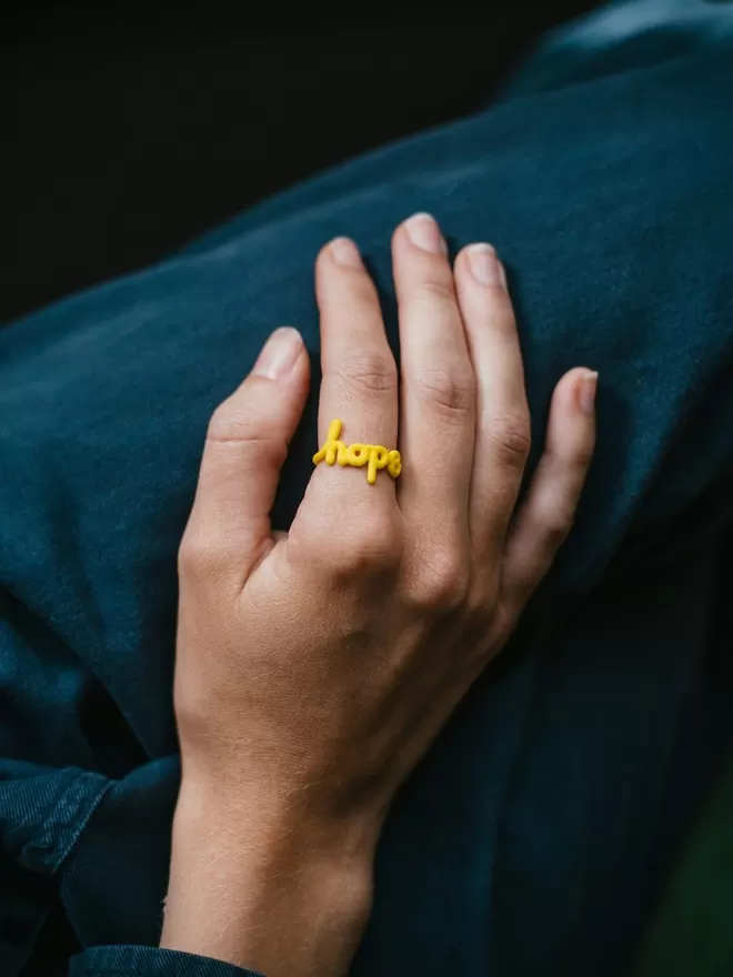 'Hope' Ring in yellow seen on a hand.