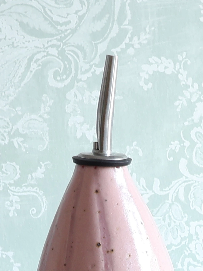 Close-up photograph of a Handmade Ceramic Stoneware Oil Pourer in Pink Stripe against a pale blue and white patterned background 
