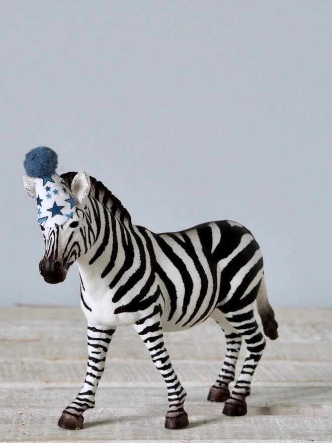 Zebra seen standing alone with a blue party hat.