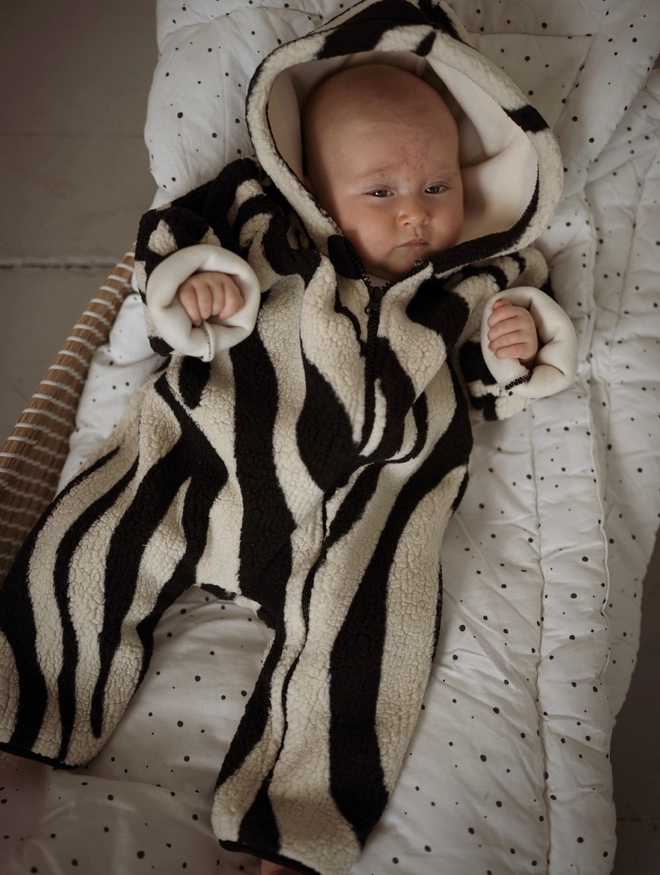 Another Fox Tiger Sherpa Baby Pramsuit seen on a baby lying in a cot on spotted bedding.
