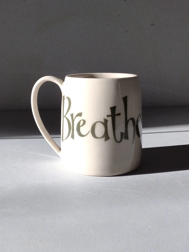 breathe large hand-thrown ceramic mug. white mug emblazoned with 'breathe' painted in large letters photographed in light to create shadows.