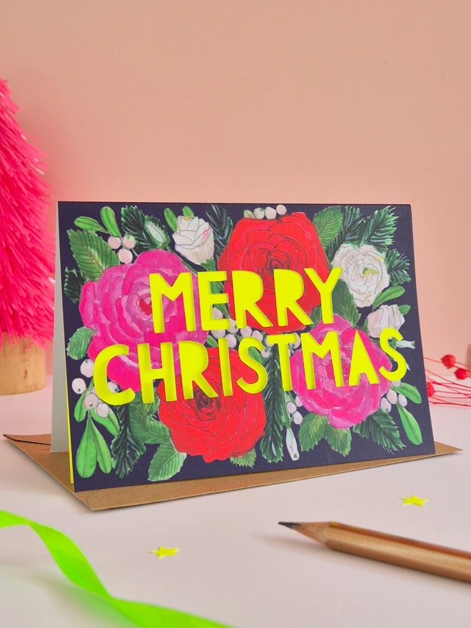 Christmas Card with roses painted on it and a paper cut Merry Christmas Slogan backed with yellow neon paper 
