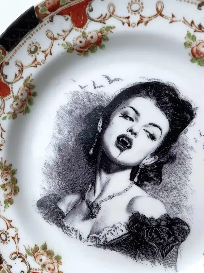 A vampire with bats behind her, the image is victorian in black and white and is printed directly onto an ornate vintage plate