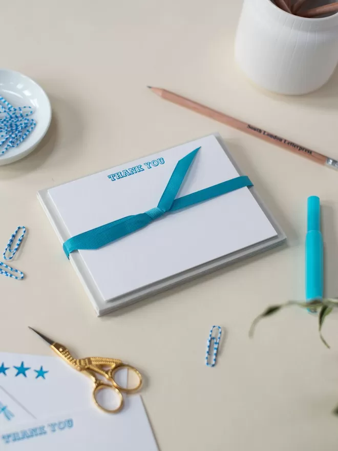 Neon Blue Thank You Cards by South London Letterpress seen tied in a blue bow with other blue stationary.