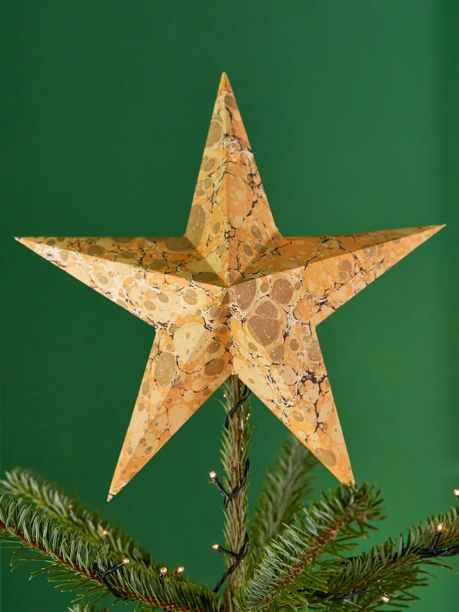 Orange and gold toned marbled paper star tree topper, on top of a Christmas tree against a green background