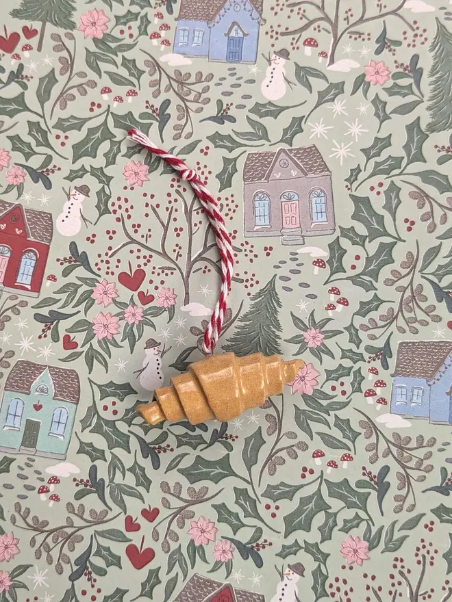 ceramic croissant hanging christmas decoration. a close up image of a small ceramic croissant hanging from red and white thread.