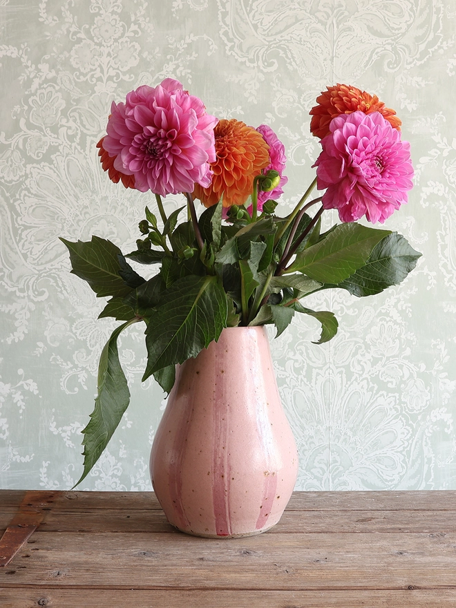 Handmade Ceramic Stoneware Large Vase in Pink Stripe filled with a bouquet of orange and pink flowers sat on a wooden surface. 