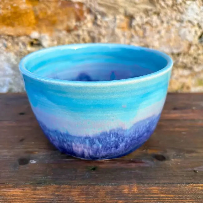 Landscape Small Bowl, a colourful bowl sitting on a wooden surface against a brick backdrop. 
