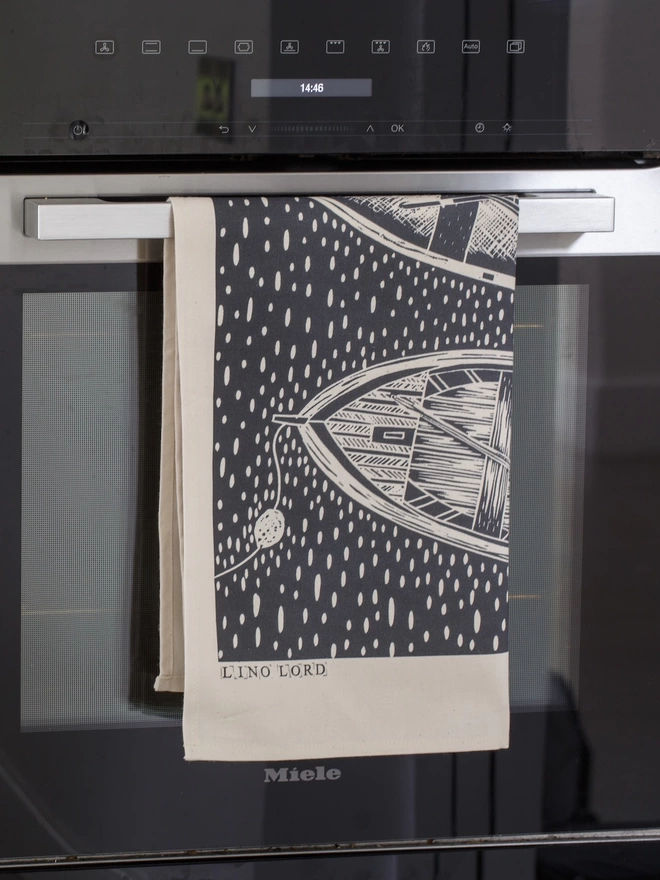 Picture of a tea towel in a kitchen with an image of 3 rowing boats, taken from an original lino print