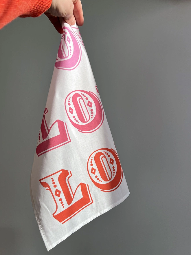 A white hand holds a Mr.PS Love Love Love Handkerchief against a white wall