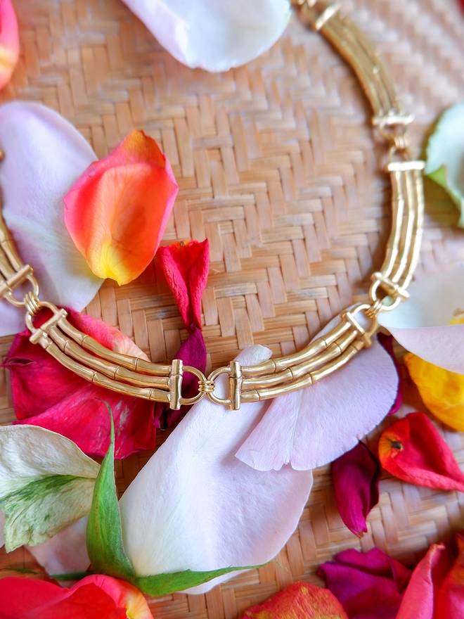Gold vermeil bamboo bar sectional collar necklace on woven basket background with rose petals