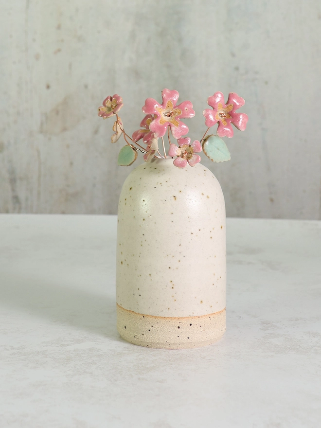 white stoneware vase with a posy of ceramic pink flowers of various sizes sits on a white marble counter top