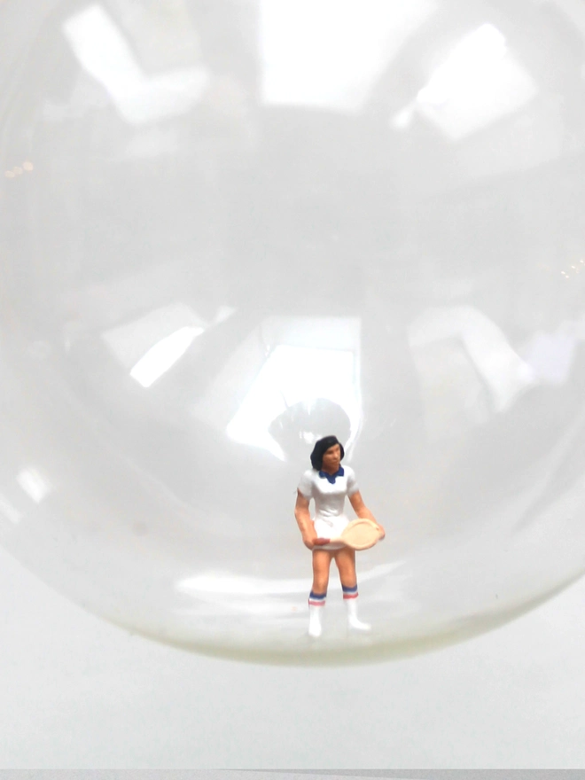 Miniature figure of a female tennis player in a glass Christmas bauble - close up 