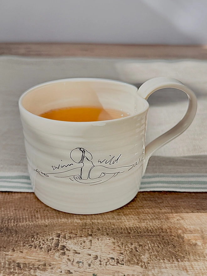 Handcrafted porcelain ‘Swim Wild’ mug – unique ceramic coffee cup for swimmers, nature lovers, and outdoor adventurers.