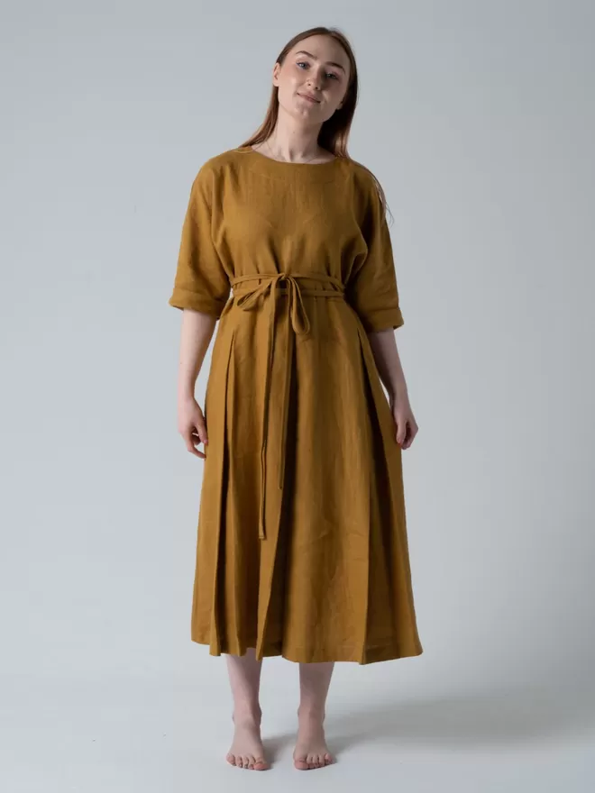 Midi length linen dress with self tie belt. Pleated skirt , elbow length sleeves. Studio view cinched waist.