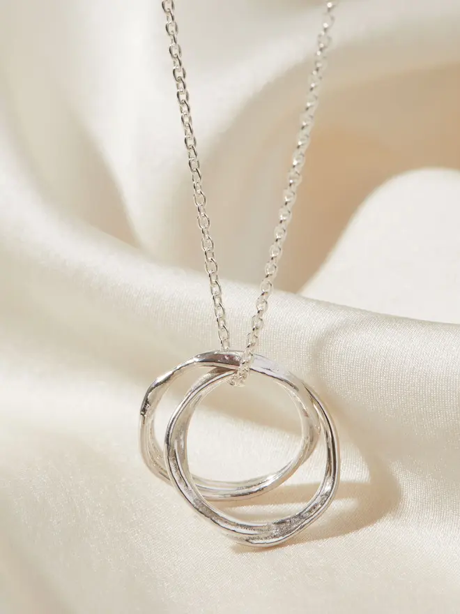 Silver Entwined Circles Necklace draped over a silk material