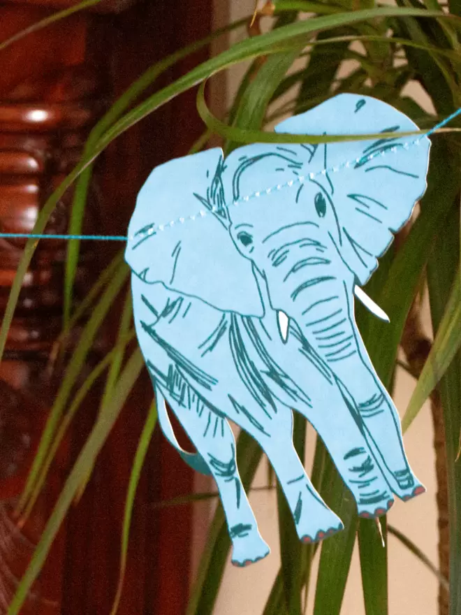 Light blue elephant with greenery in background