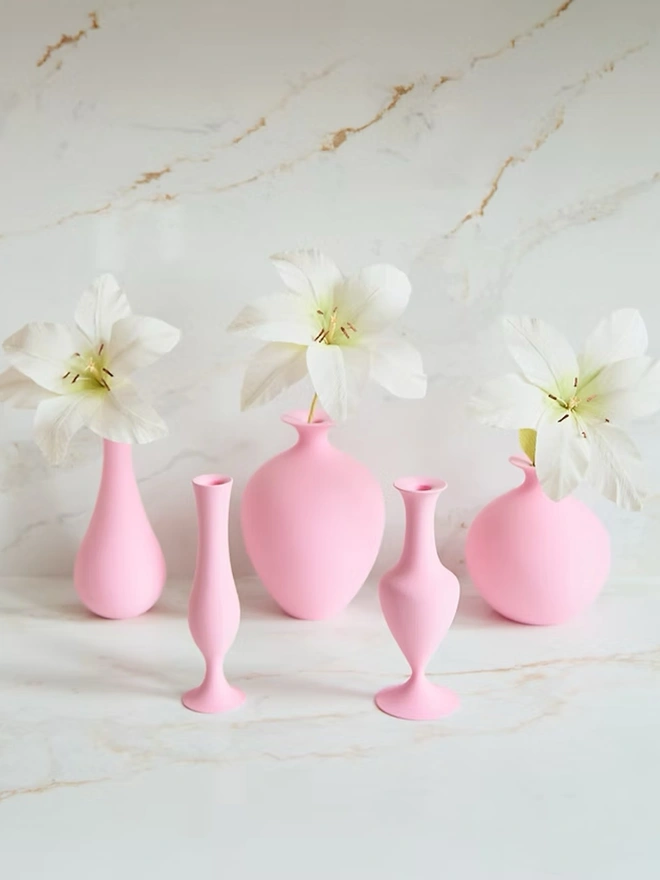 collection of various shaped pink vases with white flowers all on a white counter top