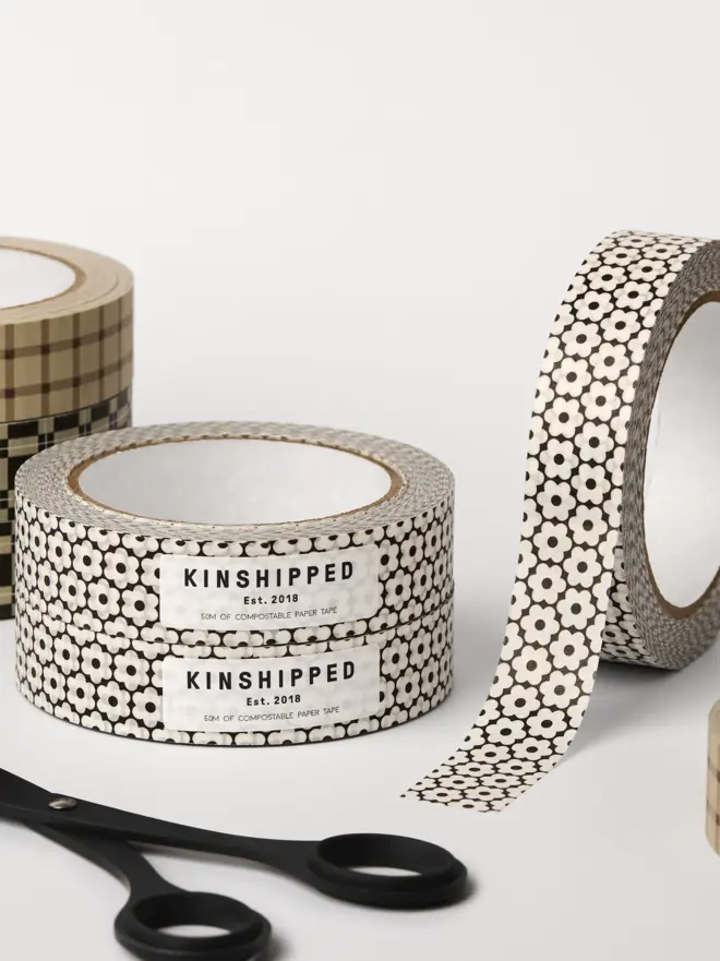 A black and white flower pattern on 5om of sticky paper tape. Tape placed behind a pair of black scissors on a white table. 